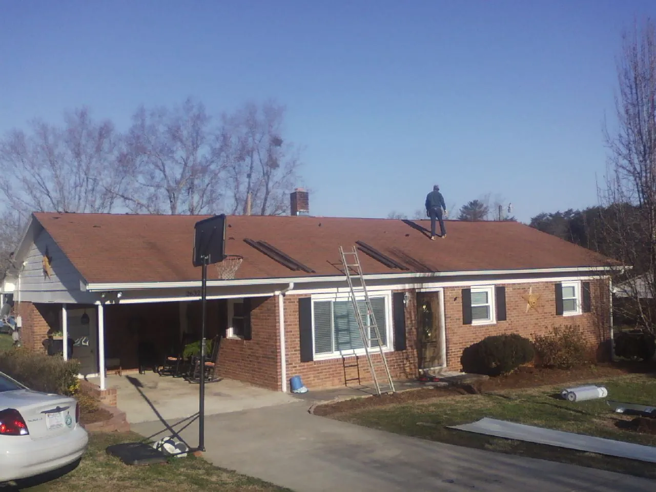 Roofer stripping a shingle roof on a brick ranch before metal panels in Newton